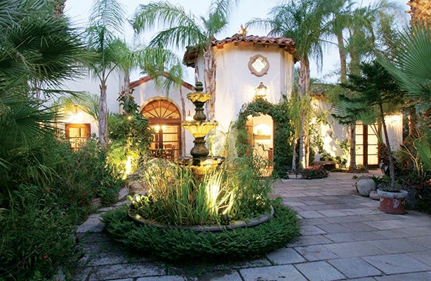 Spanish revival estate with lights on, water fountain and courtyard
