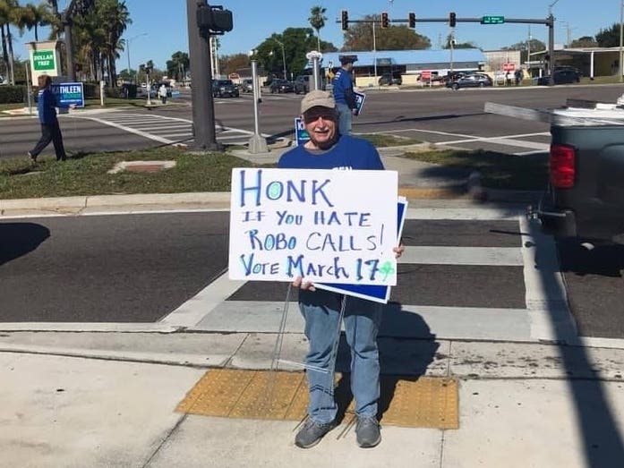 Candidates said underhanded campaign tactics have included deceptive robocalls. Gary Baker holds a sign asking fellow Clearwater residents what they think.