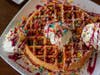 The Fruity Pebbles Waffle is made with Belgian waffle batter filled with Fruity Pebbles cereal, topped with raspberry and vanilla glaze and garnished with a dollop of cream cheese icing.