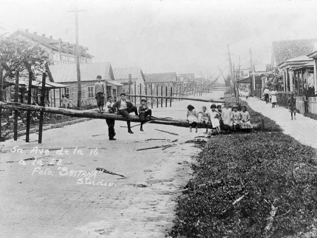 A black-and-white picture taken in 1921 shows children sitting on telephone poles that were knocked down into 5th Avenue in Ybor City by the hurricane.
