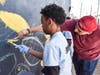 A Graffiti Park Las Vegas artist guides a young Downtown Boys & Girls Club member on painting the mural on one of the exterior Club walls.