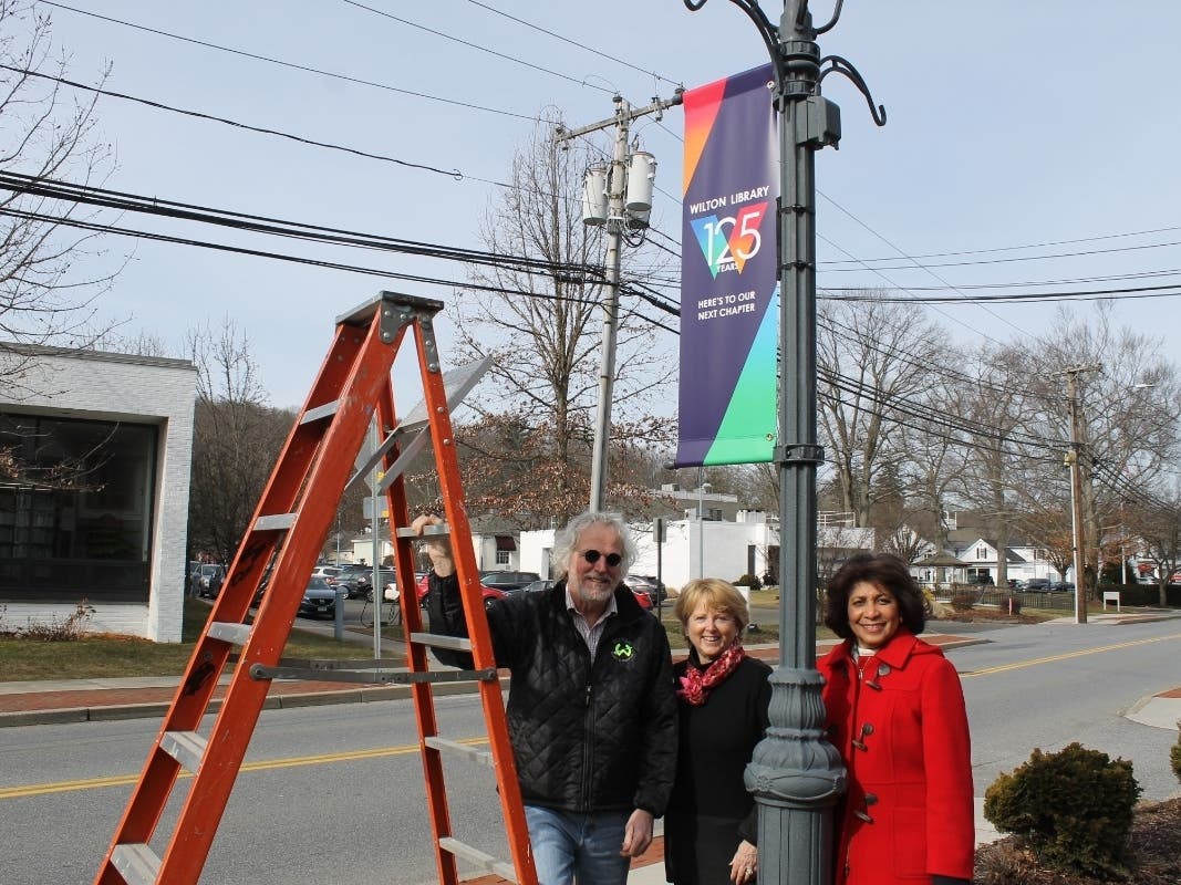 Wilton Parks & Recreation Director Steve Pierce, First Selectwoman Lynne Vanderslice, and Elaine Tai-Lauria, executive director of Wilton Library, gather as the library’s 125th Anniversary banners are placed on lampposts throughout Wilton Center.