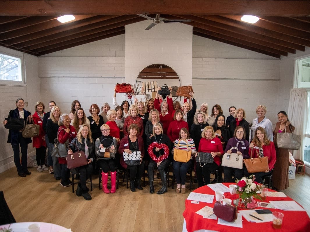 DPWC members pose at Community House with some of the many gently used handbags donated to Handbags for Hearts, founded by member Lucinda Lambros (at center holding heart). 