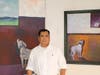 Stanley Gavidia standing in front of his paintings "Is the Sky Really Blue" (oil on canvas) and "The Things We Left Unsaid" (oil on canvas)