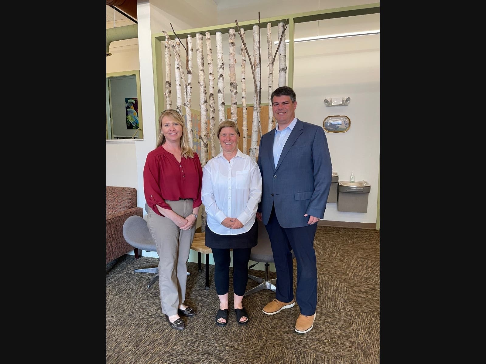 Persons standing and smiling for a photo, birch trees in the background. 