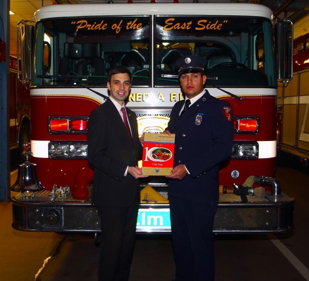 Gabriel Marques presents the Lisbon VFD centennial yearbook to Mineola FD 1st Lt. Danny Magalhaes in front of Engine 3.
