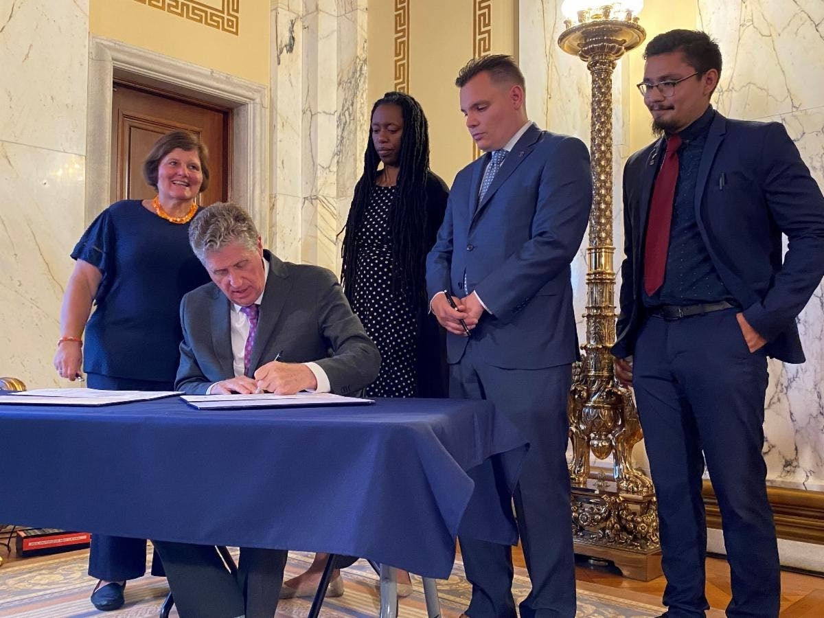 Governor McKee signs a bill which will permanently require the state to analyze overdose deaths to help identify ways to reduce their prevalence, surrounded by state leaders and activists. 