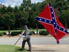 A man holding the Confederate flag stands on the side of the road along the Old Soldiers Day parade route in August.