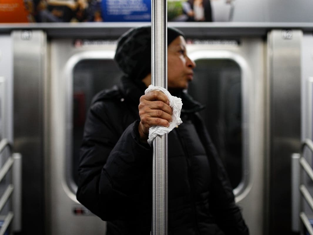 A subway customer uses a tissue to protect her hand while holding onto a pole Thursday as COVID-19 concerns drive down ridership.