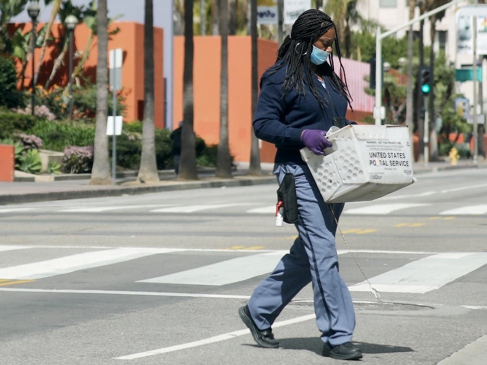 A U.S.Postal Service worker wears a face mask and gloves Tuesday while crossing a downtown street in Los Angeles, California, as the coronavirus pandemic continues.