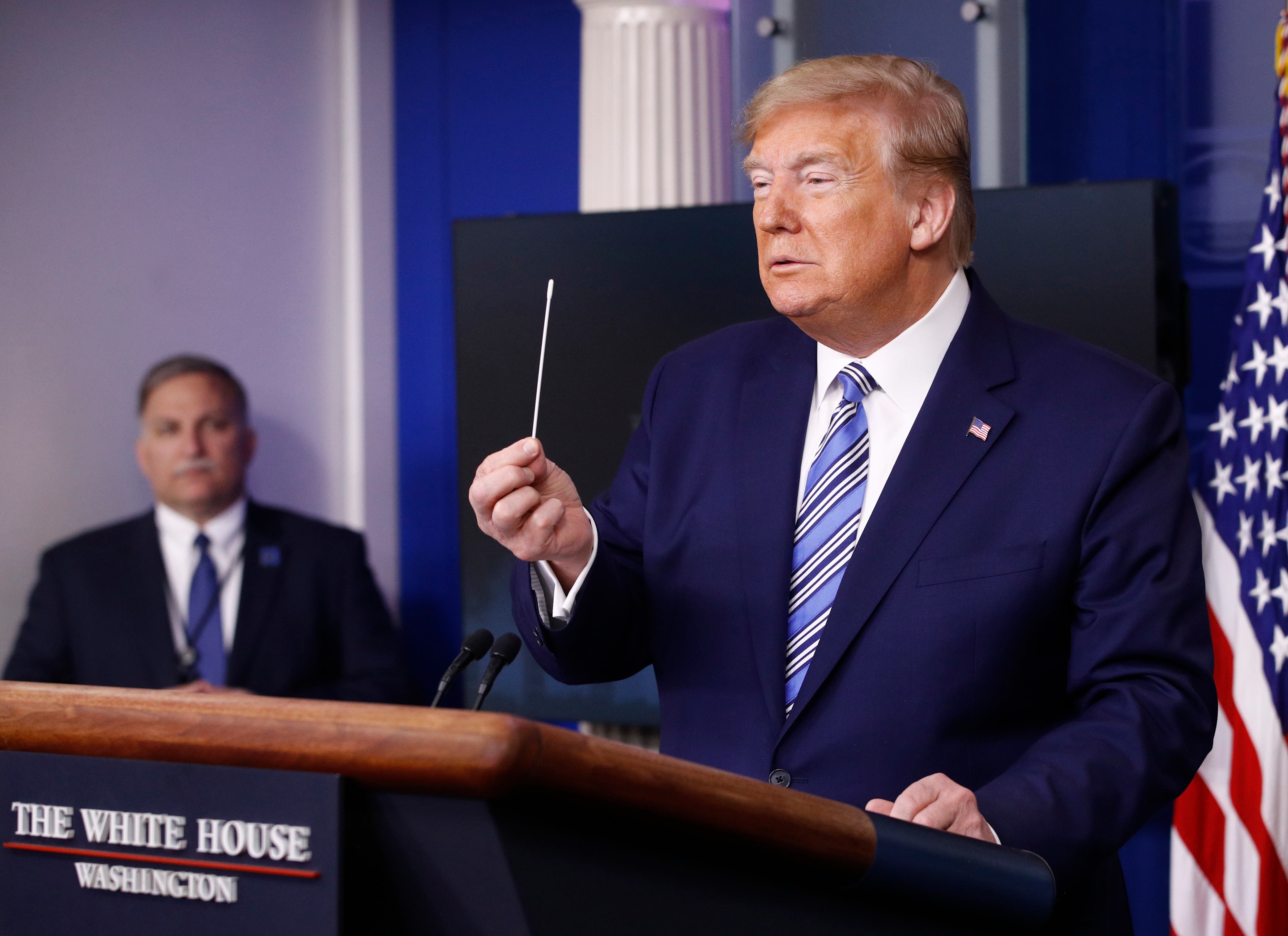 President Donald Trump holds a swab that could be used in coronavirus testing as he speaks during a coronavirus task force briefing at the White House.