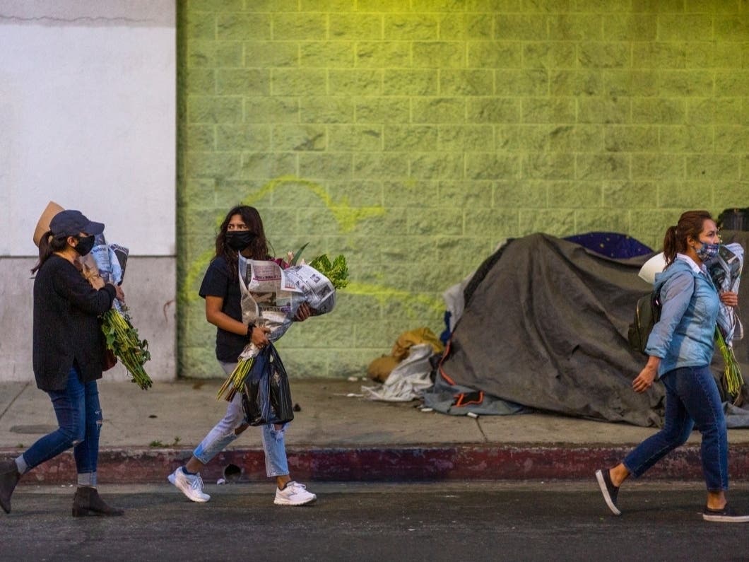 Flower buyers walk near a sidewalk homeless encampment.