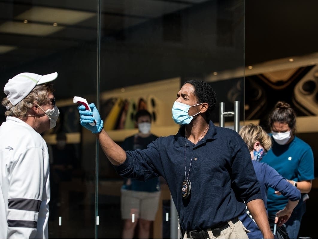 A security guard checks a customer's temperature outside an Apple Store.