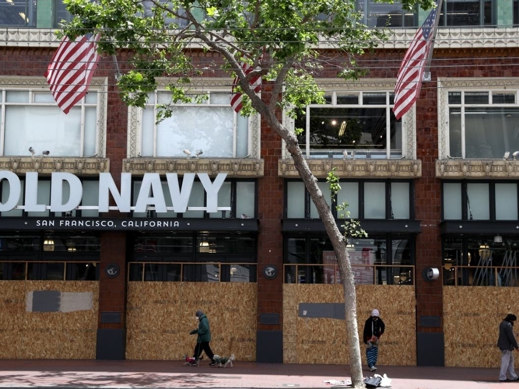 Pedestrians walk by a boarded-up Old Navy store.