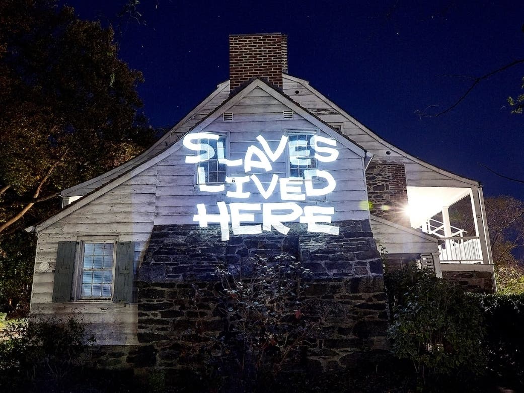 An image of the words "Slaves Lived Here" projected across the Dyckman Farmhouse Museum.