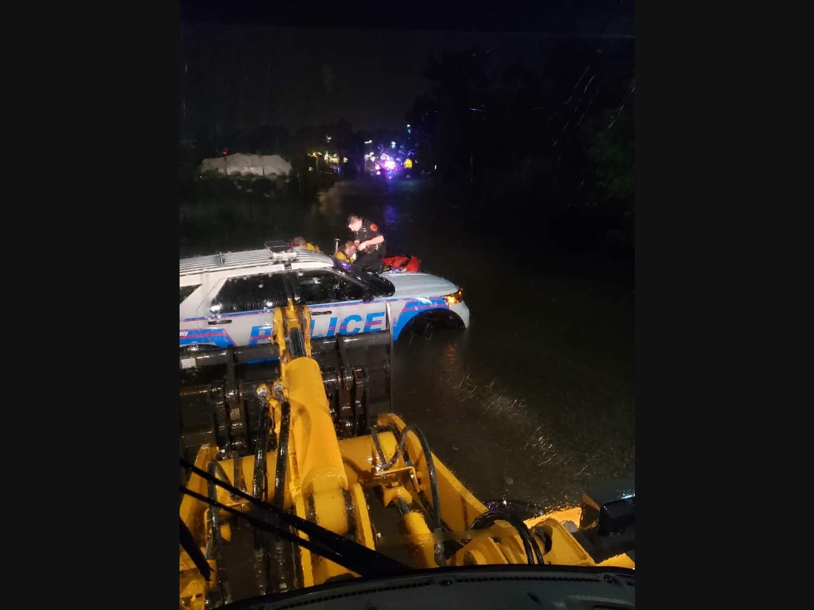 Huntington Sewage Treatment Plant staff use a payloader to assist an officer on the hood of a police vehicle stuck on flooded Creek Road as Huntington Fire Department responds with an inflatable rescue boat. 