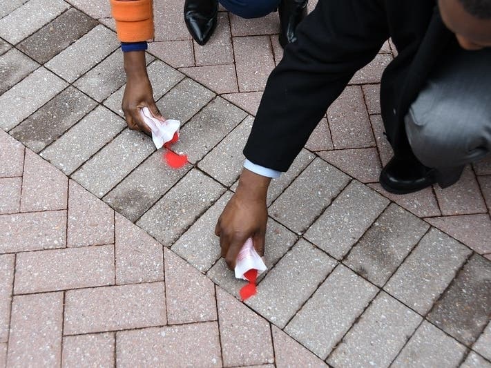 The pouring of red sand into the cracks of sidewalks is intended to “represent people who fall through the cracks of our social, economic and political systems, or those of our personal consciousness."