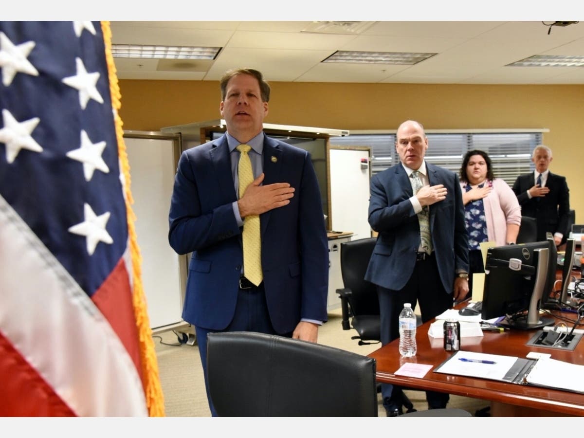 Gov. Chris Sununu is pledging allegiance to the flag at the start of Wednesday's Executive Council meeting. He is at the emergency operations center in Concord with Perry Plummer, Assistant Safety Commissioner, Fallon Reed, HSEM Chief of Planning and Atto