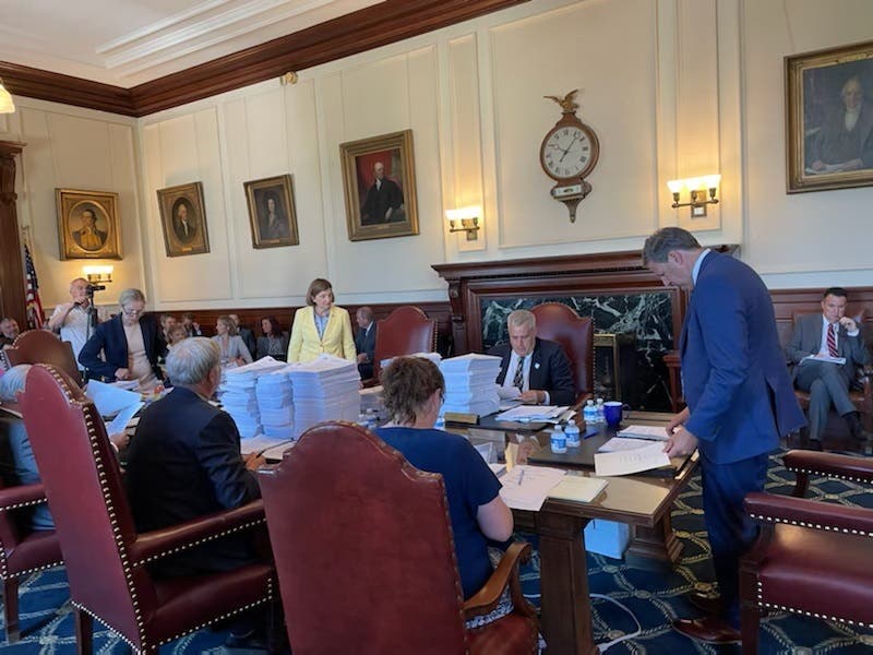 Executive Councilor Cinde Warmington, (standing wearing yellow suit) and Gov. Chris Sununu, with Executive Councilor Joe Kenney pictured seated between them, are pictured at Wednesday's Executive Council meeting.