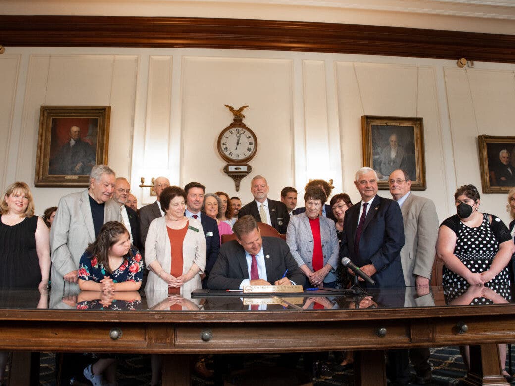 Gov. Chris Sununu signs SB 422 providing dental benefits for Medicaid recipients Friday while a bipartisan group of lawmakers and supporters look on.
