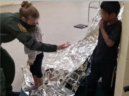 An agent comforts the siblings by the fort they made from disposable mylar blankets.
