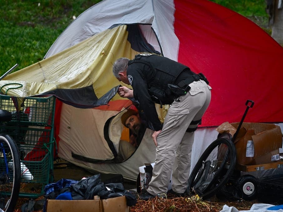 As the rain comes down, Westminster Police Department Cmdr. Kevin MacCormick talks to Jason, a homeless man living near the Beach Boulevard on-ramp of the 22 Garden Grove Freeway, after giving him a hot meal.