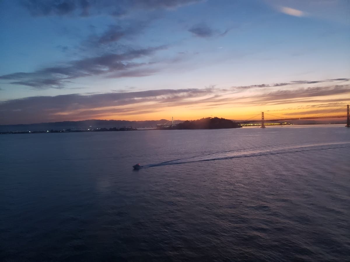 The sun coming up behind the East Bay hills, with the San Francisco-Oakland Bay Bridge in the foreground.