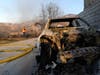 A vehicle lays destroyed from the flames of the Tick fire while a SoCal Gas worker assesses the damage of a nearby home in the Santa Clarita area of Los Angeles, Calif. on Thursday, Oct. 24, 2019