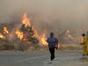 A man walks along Sierra Highway as flames from a wildfire overtake a hillside Thursday, Oct. 24, 2019, in Santa Clarita, Calif.