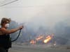 Patricia Dennison uses a hose to try to stop an advancing wildfire from affecting her business, Dennison Automotive, along Sierra Highway Thursday, Oct. 24, 2019, in Santa Clarita, Calif.