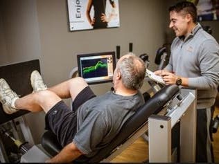 Man uses Exerbotics proprietary, AI-enabled fitness equipment (leg press) under the watchful eye of  a human coach
