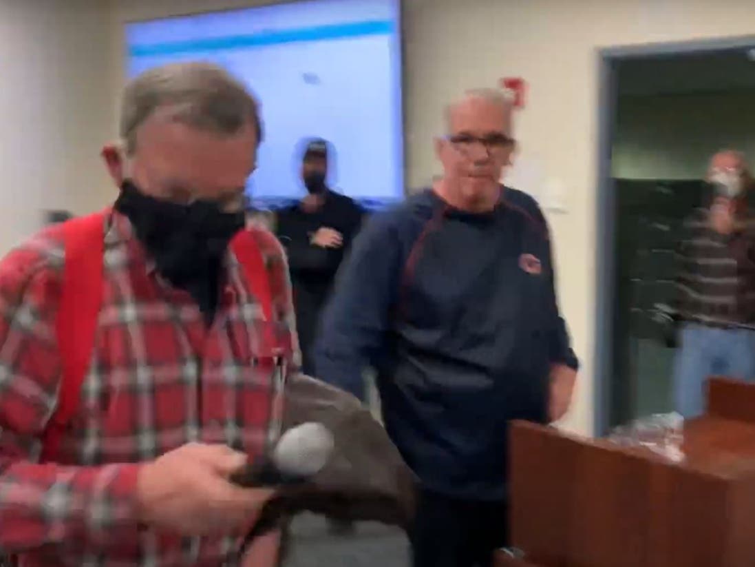 In this screenshot, Elmhurst resident Allan Fenski is removing a microphone from the podium at the Elmhurst School District 205 meeting. To the right is Elmhurst resident Paul Kenna, who spoke against mask mandates.