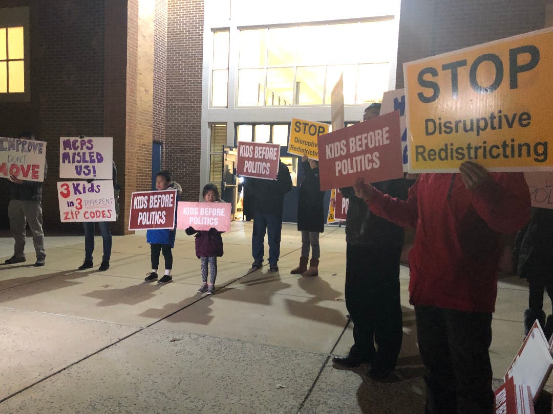 Parents hold signs in front of Gaithersburg High School ahead of the first boundary analysis meeting, showing their disapproval of the review.