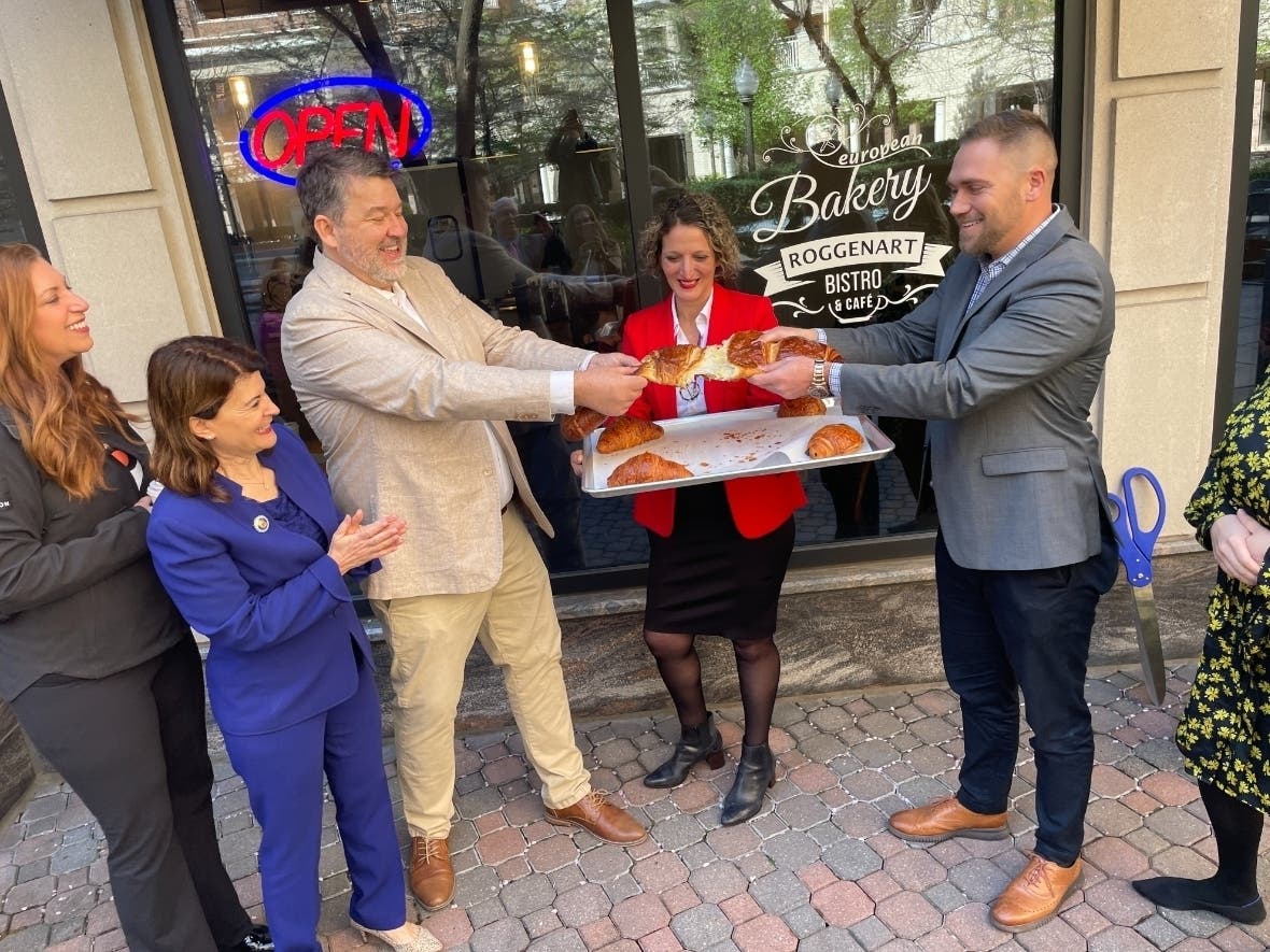 On left, Tina Leone, the CEO of the Ballston BID and State Sen. Barbara Favola (D-Ballston) watch owners Neman Popov and Brody Tennant tear apart an oversized croissant to mark the grand opening of the new Roggenart Bakery Bistro And Café in Ballston.