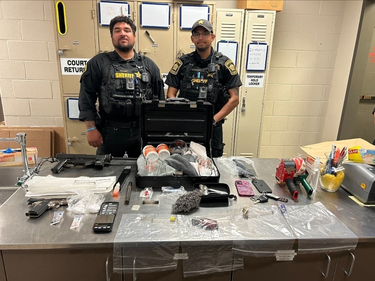 Two Spotsylvania sheriff's deputies stand next to a table filed with the narcotics, narcotics paraphernalia, and weapons recovered during the arrest of two South Carolina residents Saturday afternoon on Patriots Highway.