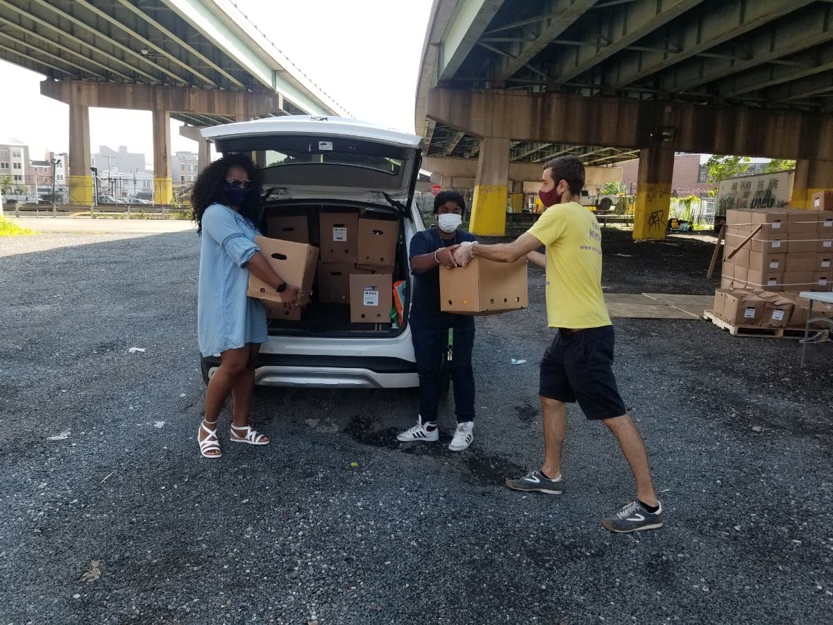 Daniel Torrance of Liberty Resources (right) hands boxes of fresh produce to Rashera Sharpe (left) and Karimah Cannon (center), both of Patterson Transportation, a LogistiCare transportation provider responsible for delivering food to those in need.