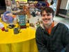 Pennsbury High School student artist Kevin Chesney kneels beside his artwork at the 2026 Tri-State Ability Art Show.