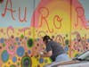 A volunteer artists paints over a boarded-up storefront Thursday in downtown Aurora.