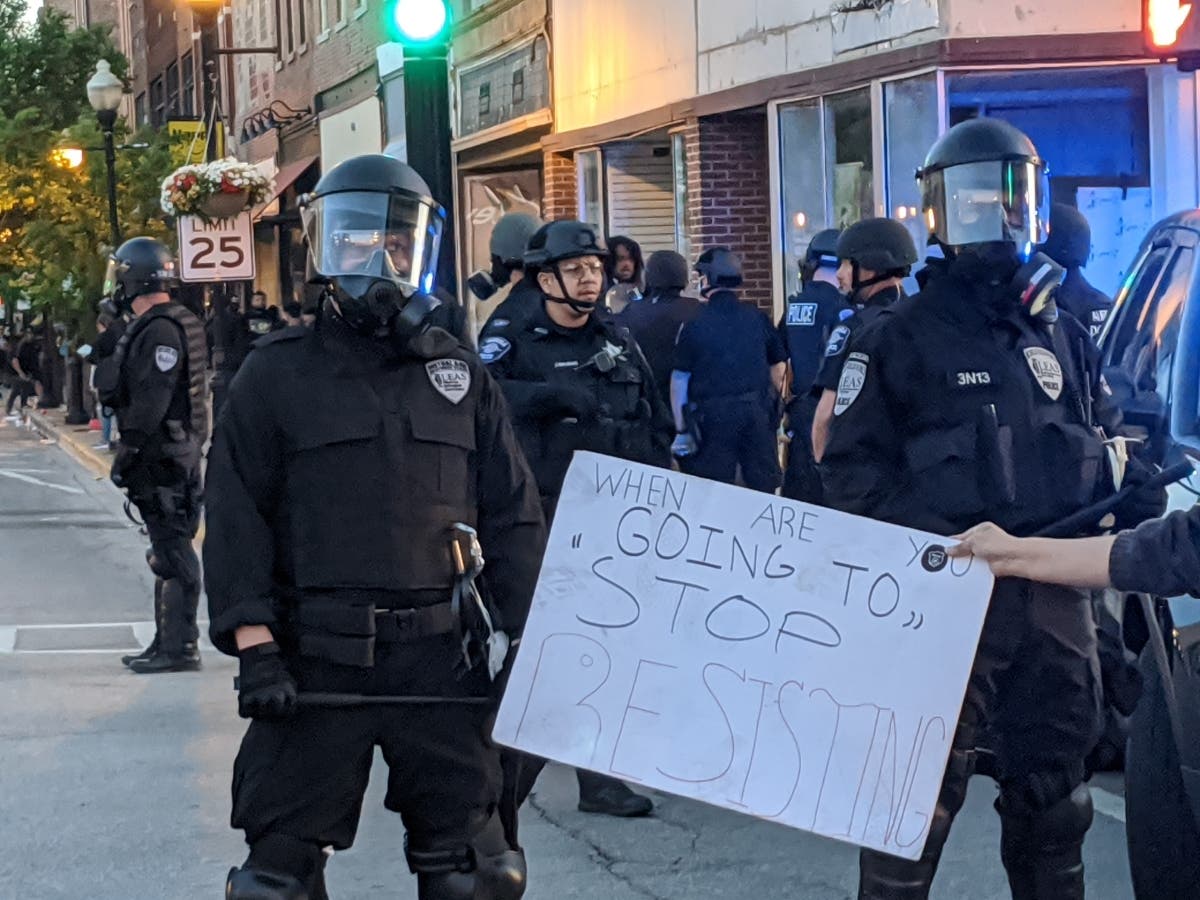 A protester holds a sign in front of police reading "When are you going to stop resisting?" during a protest May 31 in downtown Aurora. 