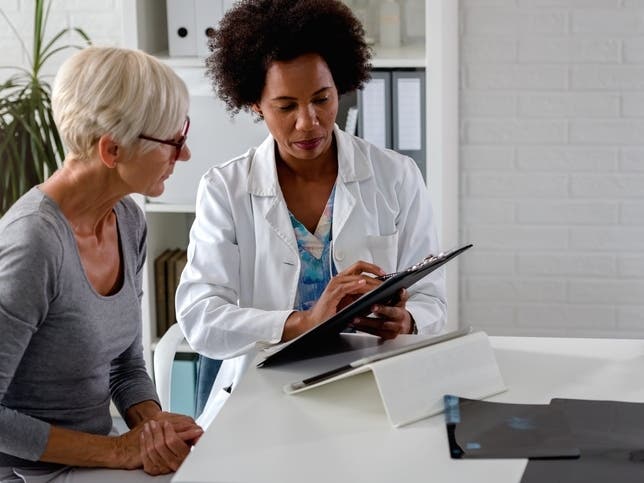 A female doctor sits at her desk and chats to an elderly female patient while looking at her  test results