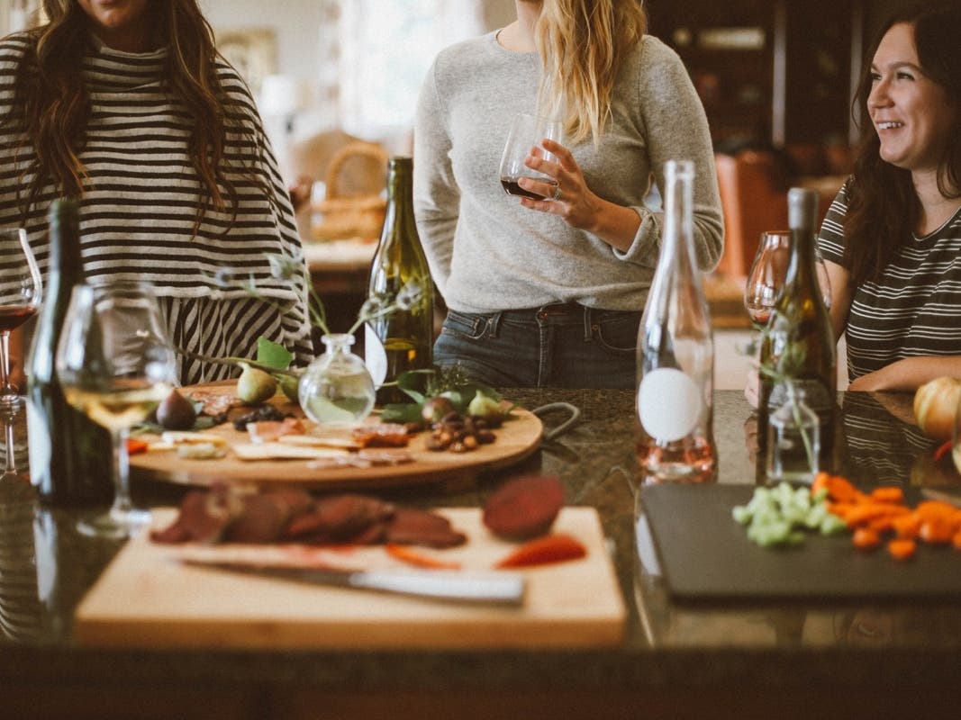 There people in the background enjoying food and drink. An array of food and wine and wine glasses in the foreground.