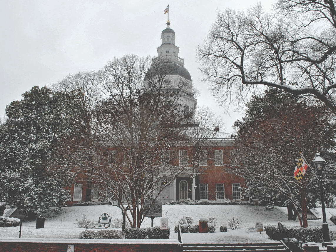 The Maryland State House shines behind snowy trees in Annapolis.