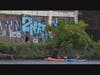 Kayakers Mary Bruno and guide Carl Alderson go past a building with graffiti situated along the Passaic River.  Photo Credit:  Scott Morris Productions