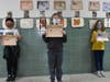 Third graders, from left, Mateo Perez, Mark Simonson and Natalie Martin display their drawings of the travel suitcases they made about the countries their ancestors hail from.