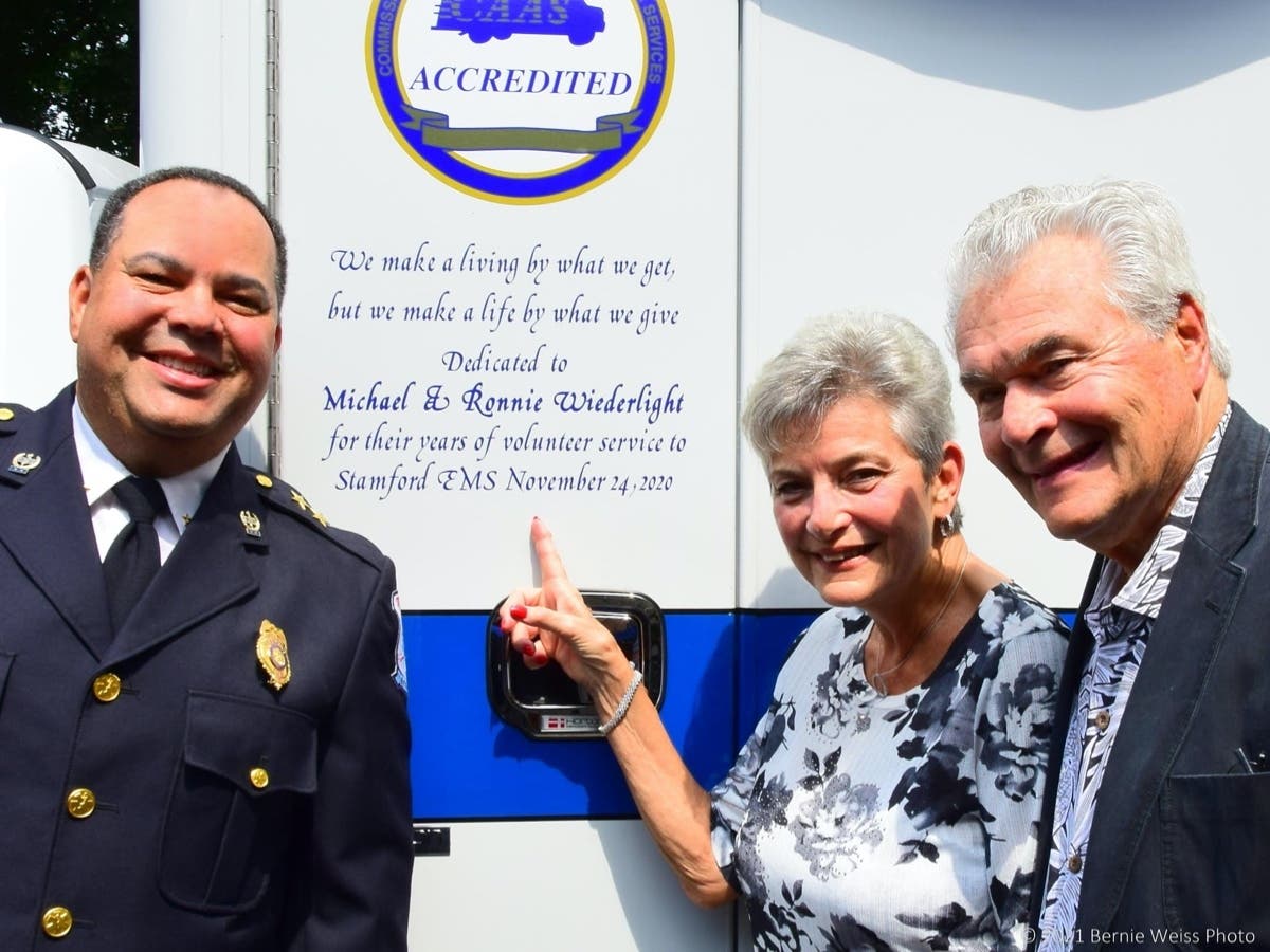 Stamford EMS Assistant Chief Edward Browne (left) Ronnie and Michael Wiederlight stand near the inscription on a new ambulance dedicated to the couple.