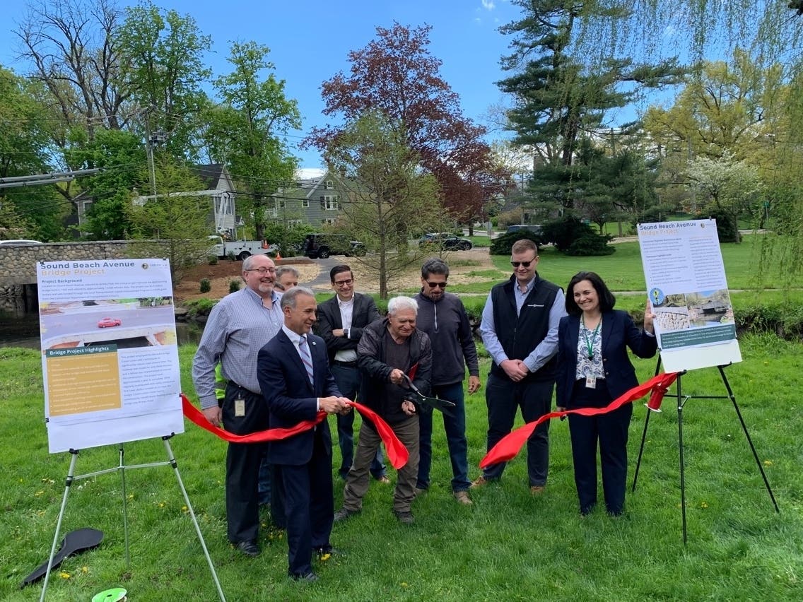 Antonio Vitti, who owns A. Vitti Excavators, the contractor for the Sound Beach Avenue bridge replacement project, cuts a ribbon to commemorate the completion of the project as town officials look on, on Wednesday, May 3, 2023.