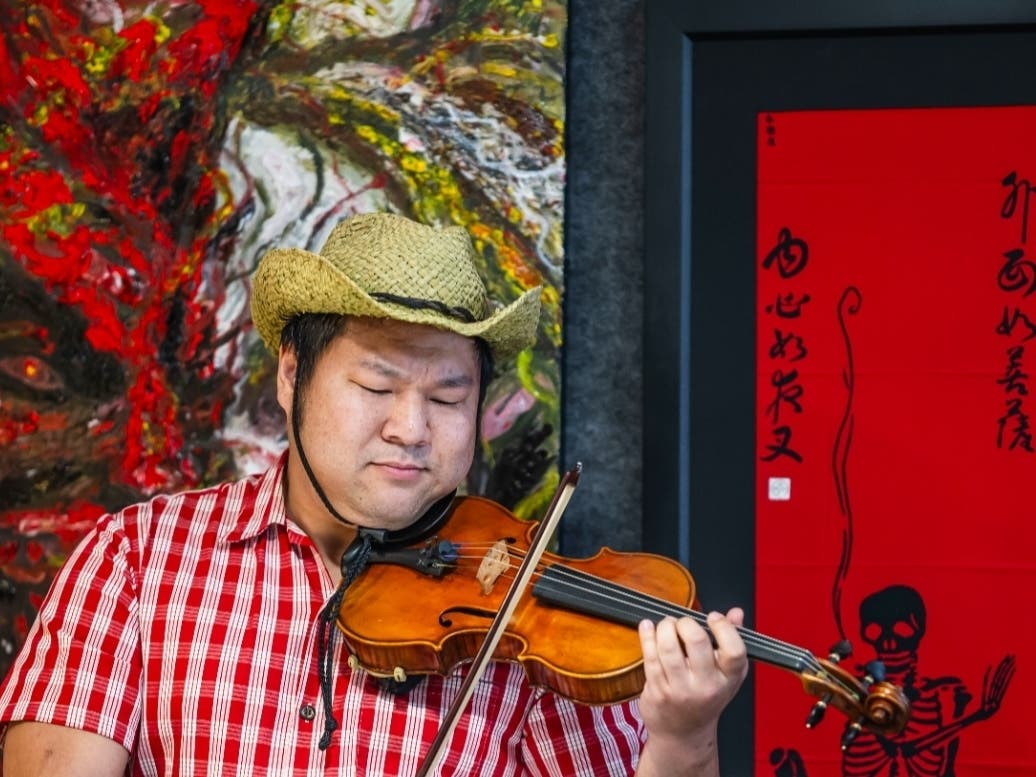 Brandon Tran, Founder of the San Ramon Valley Philharmonic, plays the violin at the opening reception of the Scary Art Show. Artwork in the background is Joseph Miguel's 'Holding My Evil In' and Adam Wolski's 'Shinigami's Tea Break'