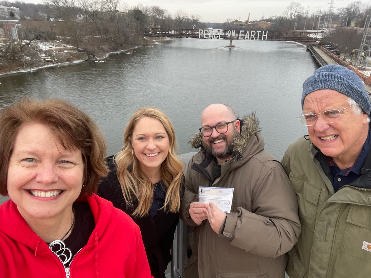 Britta McKenna, of Batavia Parks Foundation (left); Lindsay Cochrane, of Dunham Foundation; Stefin Steberl, of Batavia Parks Foundation; and Craig Foltos, Peace Bridge founder stand in front of the "Peace on Earth" sign in downtown Batavia.