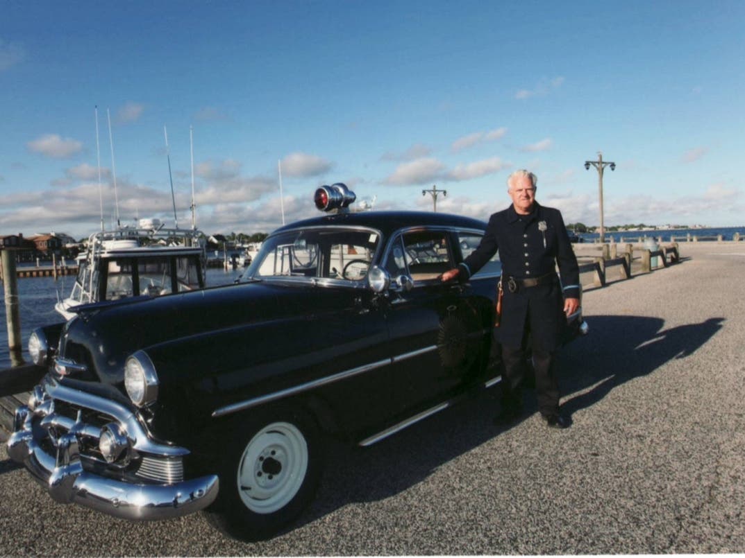 Volunteer Marty Himes poses next to the 1953 replica police car, which will lead Sunday's parade.