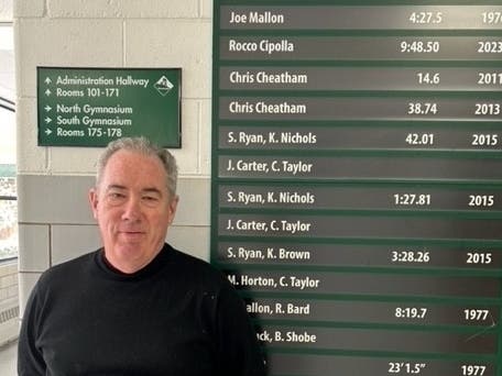 Joe Mallon is shown with the cross country record board at Evergreen Park Community High School, where his record in the one-mile run still stands today.